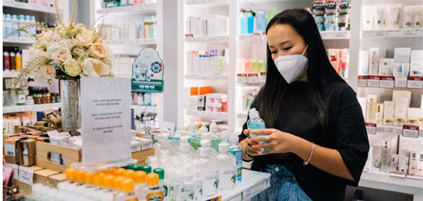 donna con mascherina all'interno di una farmacia mentre sceglie il gadget
