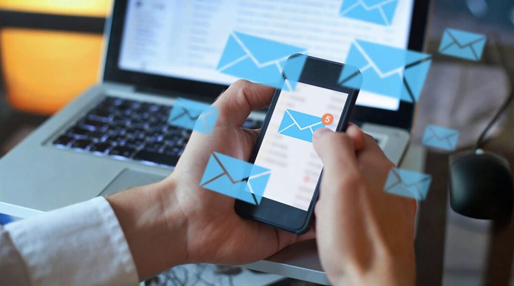 mani di uomo con smartphone che riceve email marketing con computer sullo sfondo