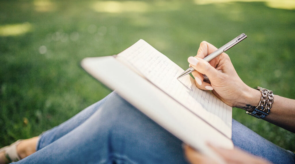 ragazza che scrive con una penna a sfera in un parco