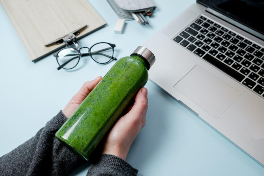 persona alla scrivania che tiene una borraccia con all'interno uno smoothie