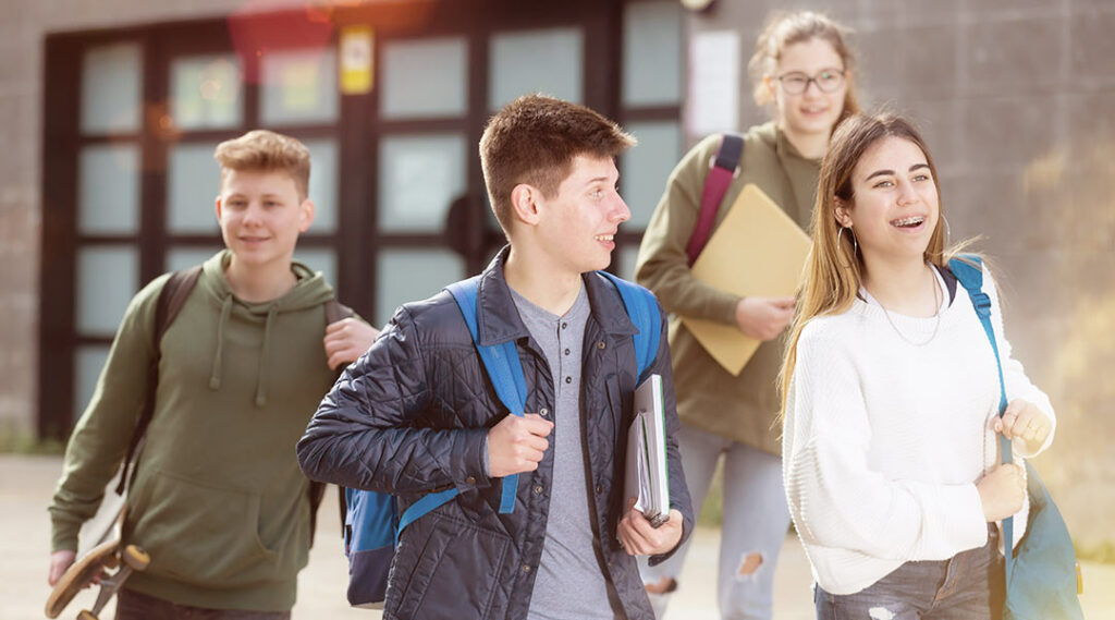 4 studenti con zaino in spalla che escono da scuola