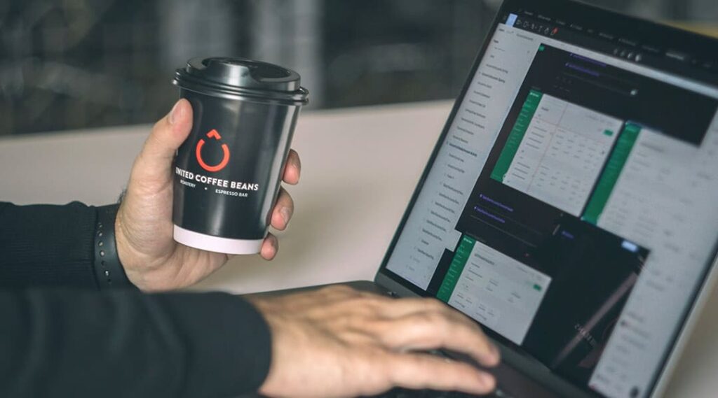 logo aziendale su un bicchiere take away tenuto da un uomo che sta al pc